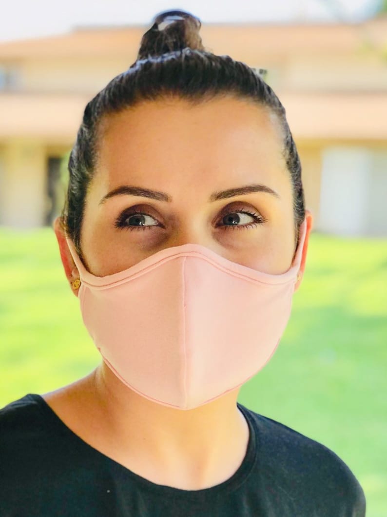 Op de afbeelding: Een persoon draagt ​​een lichtroze gezichtsmasker. Het masker is gemaakt van een zachte, ademende stof en heeft een gecontourde vorm voor een comfortabele pasvorm.