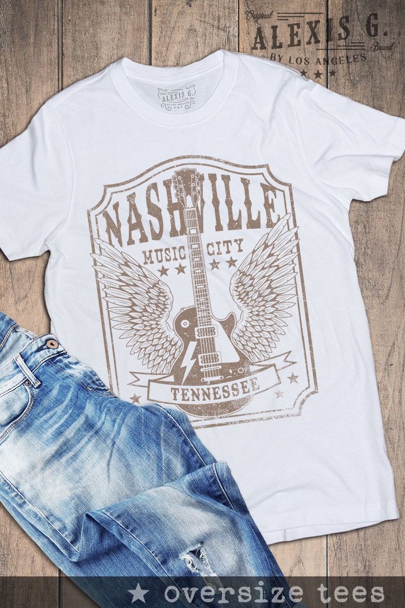May include: White t-shirt featuring a brown graphic print of a guitar with wings and the text "Nashville Music City Tennessee".