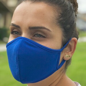 Op de afbeelding: Een persoon draagt ​​een felblauw mondkapje. Het masker is gemaakt van een zachte, comfortabele stof. De persoon draagt ​​een wit shirt met een cartoonprint.