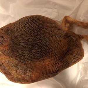 May include: A brown mesh bag with a handle, filled with what appears to be a collection of brown objects. The bag is sitting on a white surface. The bag's mesh is a light brown color.
