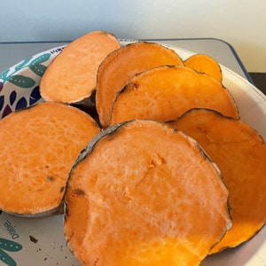 May include: A plate of sliced sweet potatoes, showcasing vibrant orange flesh and a slightly darker outer edge. The sweet potato slices are arranged on a white paper plate with a decorative blue and purple floral pattern.
