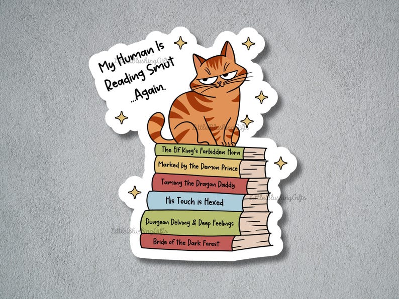 Puede incluir: Una pegatina con un gato atigrado naranja con expresi&oacute;n de enfado sentado sobre una pila de libros. Los libros tienen t&iacute;tulos humor&iacute;sticos como "Taming the Dragon Daddy". El texto encima del gato dice "My Human Is Reading Smut...Again."