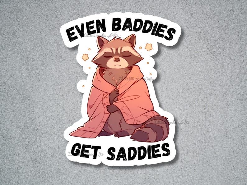 K&ouml;nnte beinhalten: Ein Aufkleber mit einem Cartoon-Waschb&auml;ren, der einen rosa Pullover tr&auml;gt, mit dem Text "Even Baddies Get Saddies".