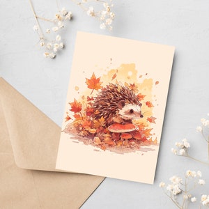 K&ouml;nnte beinhalten: Eine Aquarell-Illustration eines Igels, der auf einem Pilz in einer Waldlandschaft sitzt. Der Igel ist braun und hat einen wei&szlig;en Bauch. Der Pilz ist rot mit wei&szlig;en Punkten. Um den Igel und den Pilz herum liegen orange und gelbe Bl&auml;tter.