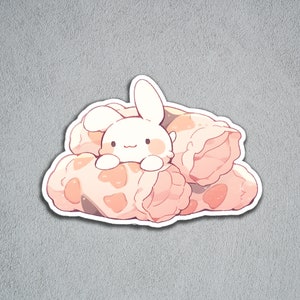 May include: A white bunny with pink cheeks peeking out from a pile of pink and brown patterned fabric rolls.