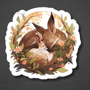 K&ouml;nnte beinhalten: Ein Aufkleber mit einem braunen Fuchs und einem wei&szlig;en Kaninchen, die zusammen in einem Kreis aus gr&uuml;nen Bl&auml;ttern und rosa Bl&uuml;ten schlafen.