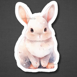 May include: A white watercolour bunny with brown eyes and a pink nose. The bunny is sitting with its paws tucked under its body. The background is a soft, watercolour wash of blue and pink.