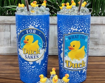 May include: Two blue tumblers with white speckles and duck-themed graphics. One says "For Duck Sakes" and the other says "What the Duck". Each has a metal straw and is decorated with yellow rubber duckies and clear glass beads.