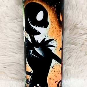 Puede incluir: Un vaso cil&iacute;ndrico con un dise&ntilde;o de Jack Skellington de Pesadilla antes de Navidad, sobre un fondo naranja y negro. El dise&ntilde;o incluye otros personajes y elementos de la pel&iacute;cula.
