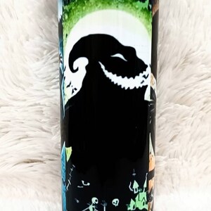 Puede incluir: Un vaso cil&iacute;ndrico con un dise&ntilde;o de Pesadilla antes de Navidad. El vaso negro tiene una luna blanca, una silueta de Oogie Boogie e im&aacute;genes de Jack Skellington y otros personajes. El fondo tiene un degradado verde y negro.