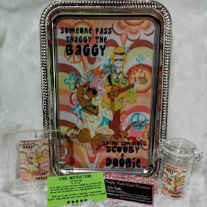 May include: A decorative metal rolling tray with a colorful cartoon design featuring Shaggy, Scooby-Doo, and the text "Someone pass Shaggy the Baggy so he can roll Scooby a Doobie." Also included is a small glass jar and a small card with the same design.