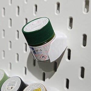 May include: A small, clear glass bottle with a green lid and a white label. The label reads "FLAT GREEN XF-5". The bottle is hanging on a white pegboard.