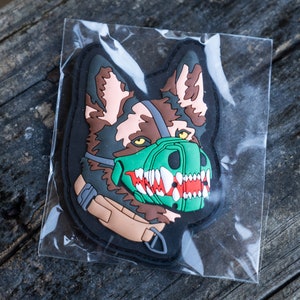 Peut inclure: Un patch de chien brun et noir avec un museau vert et rouge. Le patch est dans un sac en plastique.