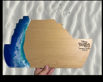 May include: Wooden serving board shaped like a cruise ship, featuring a blue and white resin wave design on the left. The board is engraved with "Disney Destiny" and "Inaugural Season 2024" on the right side.
