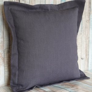 Könnte beinhalten: Ein quadratisches, anthrazitfarbenes Leinenkissen mit einem kontrastierenden Rand. Das Kissen hat ein weiches, strukturiertes Aussehen und ein schlichtes, elegantes Design. Das Kissen ist etwa 50 cm groß.