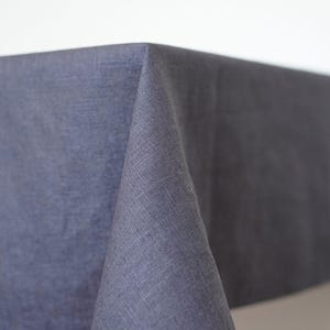 Könnte beinhalten: Nahaufnahme einer dunkelblauen Leinentischdecke. Der Stoff hat ein strukturiertes Aussehen und ist über einen Tisch drapiert. Die Ecke der Tischdecke ist fokussiert und zeigt das Gewebe des Stoffes.