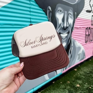May include: A brown and white trucker hat with the text "Silver Springs MARYLAND" in cursive script.