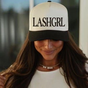 May include: A white and black baseball cap with the text "LASHGRL" in black lettering on the front.