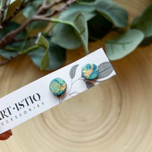 Könnte beinhalten: Ein Paar kleine, runde Ohrringe mit einem teal- und goldfarbenen Marmormuster. Die Ohrringe befinden sich auf einer weißen Karte mit dem Text "ART-ISTIQ ACCESSORIES".