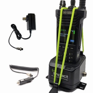 May include: A black two-way radio with a green strap is in a black charging cradle. The cradle has a power cord and a cigarette lighter adapter. The radio has a screen that displays "ESA DISP B 56.24000".