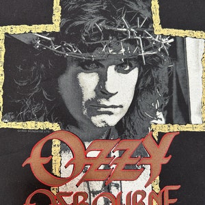 May include: Black t-shirt with a portrait of Ozzy Osbourne wearing a crown of thorns, set against a cross-shaped background. The name "Ozzy Osbourne" is displayed in a stylized font.