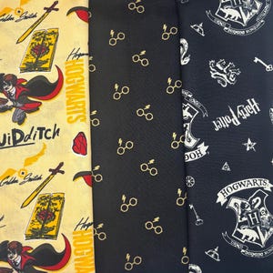 Puede incluir: Tres paneles de tela con diseños temáticos de Harry Potter. Un panel es amarillo con gráficos de Quidditch y Hogwarts. Otro es negro con gafas doradas. El tercero es azul marino con escudos y texto de Hogwarts.