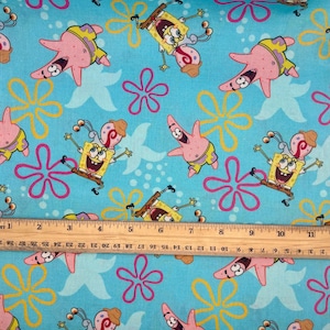 May include: A patterned fabric with cartoon characters SpongeBob SquarePants and Patrick Star, starfish, and floral designs on a light blue background. The characters are in various poses, with yellow, pink, and brown colours.