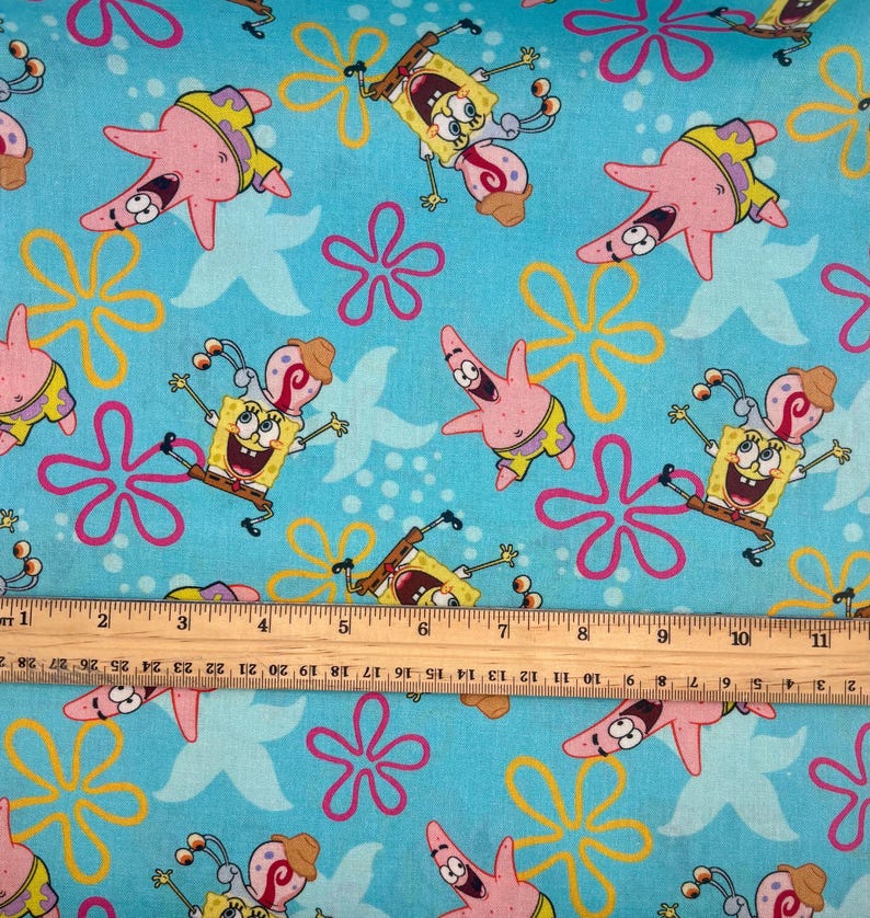 May include: A patterned fabric with cartoon characters SpongeBob SquarePants and Patrick Star, starfish, and floral designs on a light blue background. The characters are in various poses, with yellow, pink, and brown colours.