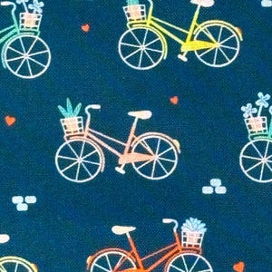 May include: Dark teal fabric with a repeating pattern of bicycles. Each bicycle has a basket filled with flowers or plants. The bicycles are in shades of yellow, orange, and pink, with white wheels and accents. Small hearts and cloud shapes are scattered throughout.
