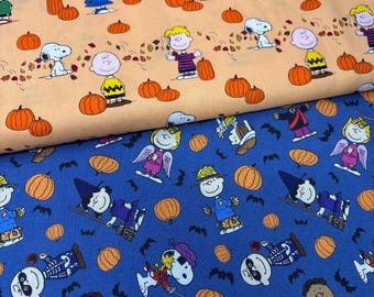 Może przedstawiać: Dwa złożone kawałki tkaniny z postaciami z Peanuts. Górna warstwa jest jasnopomarańczowa z Snoopy'm, Charlie Brownem i Lucy wśród dyń i jesiennych liści. Dolna warstwa jest niebieska z postaciami w kostiumach na Halloween i dyniami.