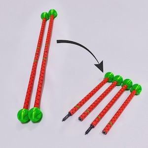 May include: Red and green drumsticks with a textured red shaft and green ball-shaped ends. The drumsticks have a green and red crisscross pattern. The image shows two drumsticks and a set of four drumsticks.
