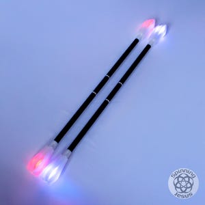Könnte beinhalten: Zwei schwarze LED-Poi mit weißen Spitzen. Die Spitzen leuchten in Rot und Blau.