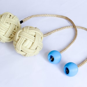 May include: Two cream-colored rope balls connected by a brown rope with two blue weighted balls on the ends of the rope.
