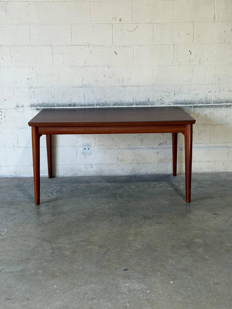 May include: A rectangular wooden dining table with a smooth, dark brown top and four tapered legs. The table features a clean, simple design with a horizontal apron connecting the legs, showcasing a consistent wood grain finish throughout the piece.