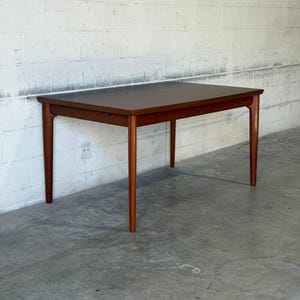 May include: A rectangular wooden dining table with a smooth, dark brown finish. The table features four tapered legs that extend from the corners, supporting a flat, solid top with clean, straight edges and a visible wood grain texture throughout.