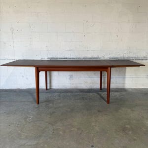 May include: A rectangular wooden dining table with a dark brown top and four tapered legs. The table features two extendable side leaves that are pulled out to increase the surface area, creating a long, flat, and smooth tabletop surface.