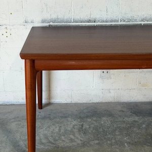 May include: A rectangular wooden table with a smooth, dark brown finish. The table features a flat top surface with slightly rounded edges and four tapered, cylindrical legs that extend downwards from the corners of the frame.