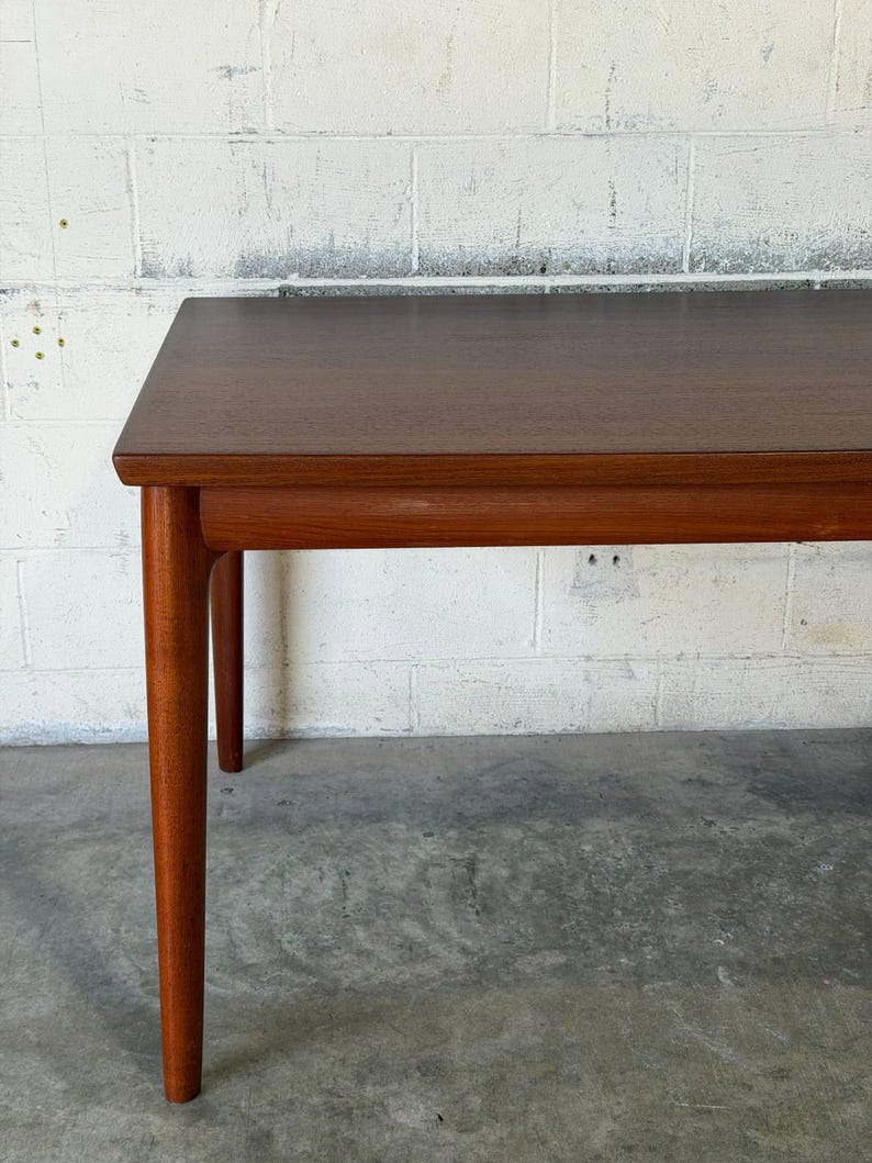 May include: A rectangular wooden table with a smooth, dark brown finish. The table features a flat top surface with slightly rounded edges and four tapered, cylindrical legs that extend downwards from the corners of the frame.