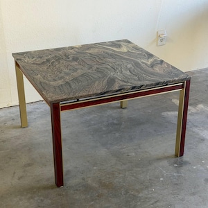 May include: Square coffee table with a patterned granite top. The table has a dark red wood frame with gold-colored metal legs. The table is approximately 24 inches square and 18 inches high.