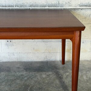 May include: A rectangular wooden table with a dark brown top and a lighter brown frame. The table features four tapered legs that extend from the corners, showcasing a smooth, polished finish and visible wood grain throughout the entire structure.