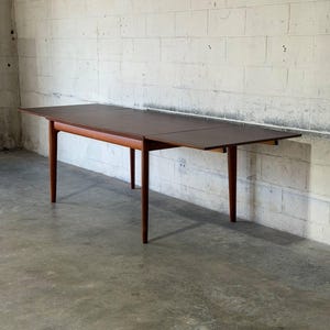 May include: A rectangular wooden dining table with a dark brown top and a lighter brown wooden frame. The table features four tapered legs and an extendable surface design, showcasing a smooth finish and clean lines throughout the structure.