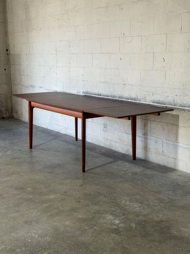 May include: A rectangular wooden dining table with a dark brown top and a lighter brown wooden frame. The table features four tapered legs and an extendable surface design, showcasing a smooth finish and clean lines throughout the structure.