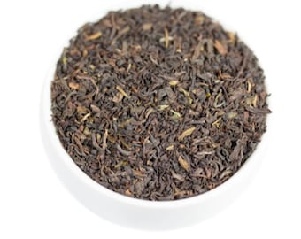 May include: A close-up of a white bowl filled with loose black tea leaves.