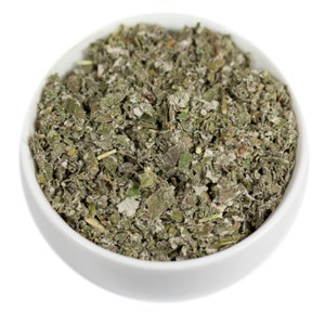 May include: A white bowl filled with dried, light green, and gray herbal leaves.