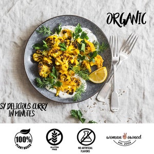 May include: A plate of roasted cauliflower florets with a creamy sauce, garnished with fresh herbs and a lemon wedge. The text "EASY DELICIOUS CURRY IN MINUTES" is written below the plate. The text "ORGANIC" is written in the upper right corner of the image.  Four icons are displayed below the plate: a green leaf with the text "100% PLANT BASED", a wheat stalk with the text "GLUTEN FREE", a flask with a diagonal line through it with the text "NO ARTIFICIAL FLAVORS", and a peace sign with the text "woman owned est. 2004".