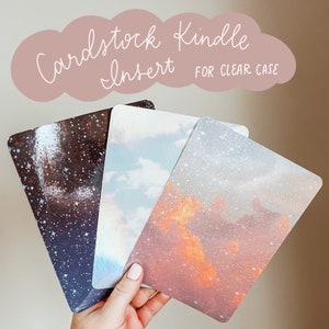May include: Four different cardstock inserts for a clear Kindle case. The inserts feature a variety of designs, including a starry night sky, a cloudy sky, and a sunset sky.
