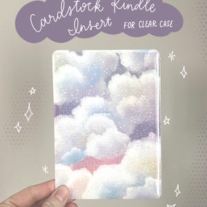 May include: A rectangular cardstock Kindle insert for a clear case, featuring a watercolor design of fluffy white and pastel-colored clouds against a starry sky. The text "Cardstock Kindle Insert FOR CLEAR CASE" is above the insert.