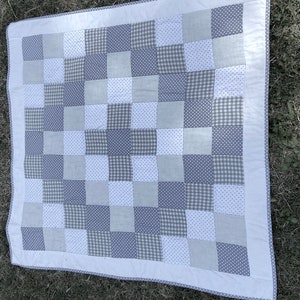 Könnte beinhalten: Eine Patchwork-Decke mit weißem Hintergrund und Quadraten in Grau, Weiß mit grauen Punkten und grauem Gingham.