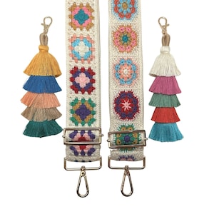 May include: Two white crocheted straps with colourful granny square patterns and gold metal clasps. Each strap has a tassel keychain with multiple layers of colourful tassels.