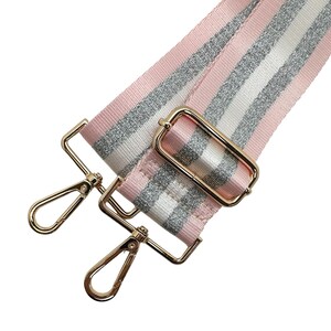 Peut inclure: Bandouli&egrave;re de sac &agrave; rayures roses, argent&eacute;es et blanches avec une quincaillerie m&eacute;tallique dor&eacute;e. La sangle pr&eacute;sente un motif r&eacute;p&eacute;t&eacute; de rayures roses, argent&eacute;es scintillantes et blanches. La quincaillerie dor&eacute;e comprend deux mousquetons pivotants et une boucle rectangulaire.